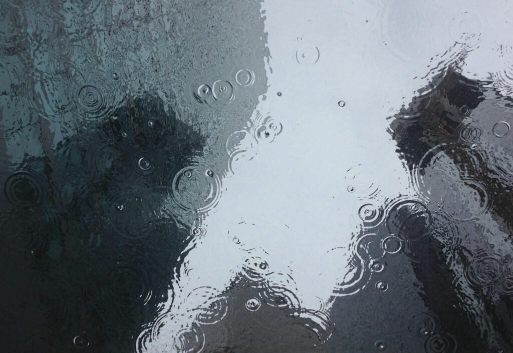 Raindrops create ripples on a window, reflecting an urban backdrop.