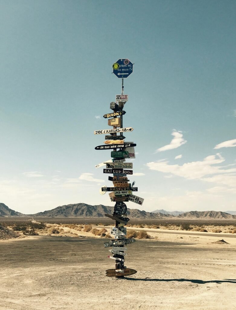 Tall signpost in a desert landscape under a clear blue sky with mountains in the background.